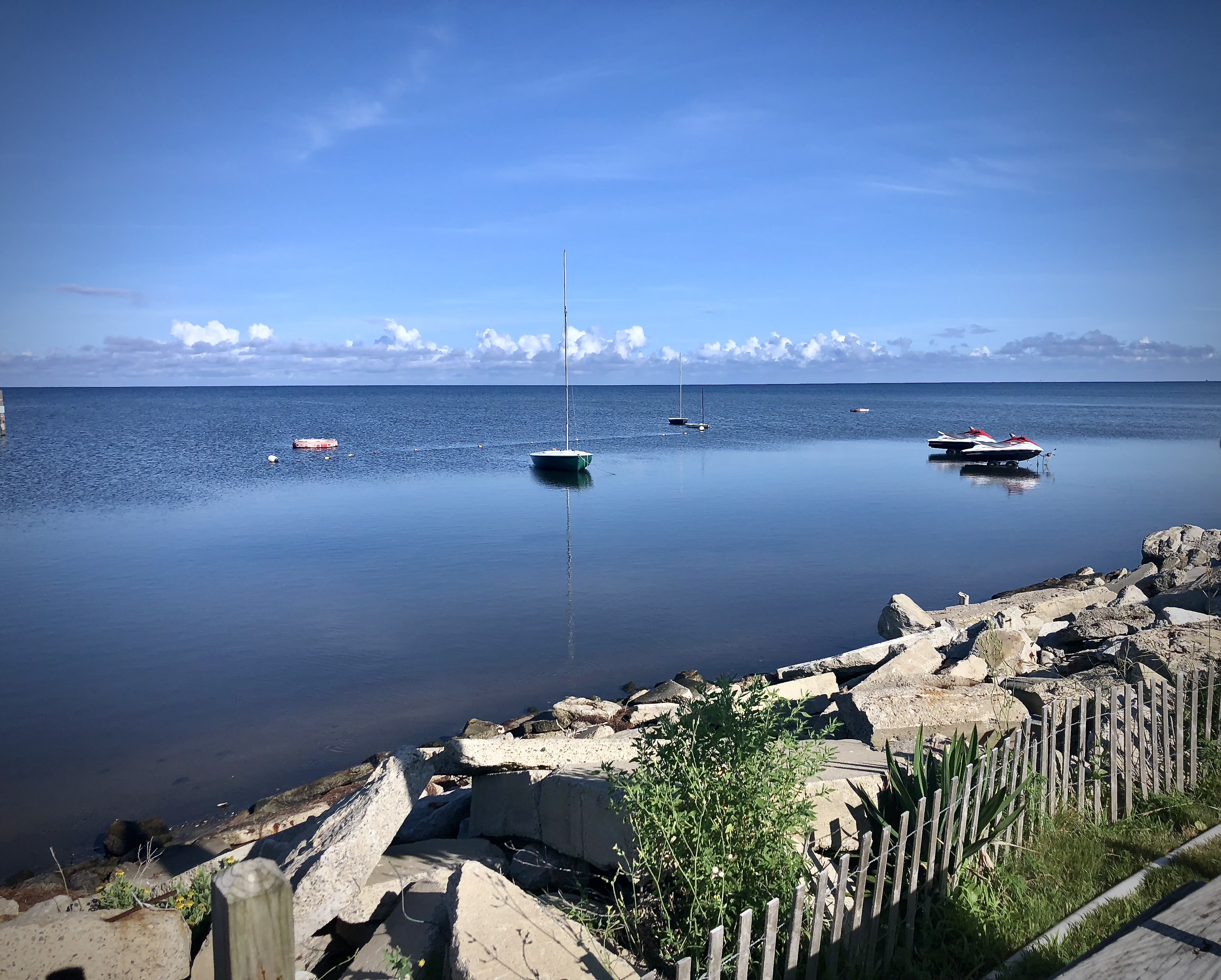 Sailboat and jet ski moored in a calm bay, seen past a broken concrete jetty